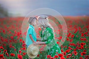 Mother with son in poppies enjoying life at sunset. Happy family summer vacation. Pretty brunette with long healthy hair holding