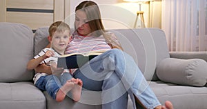 Mother and son are reading a book sitting on a cozy sofa in the living room