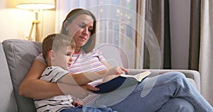 Mother and son are reading a book sitting on a cozy sofa in the living room