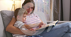 Mother and son are reading a book sitting on a cozy sofa in the living room