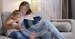 Mother and son are reading a book sitting on a cozy sofa in the living room