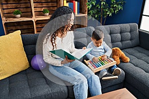 Mother and son reading book sitting on sofa at home