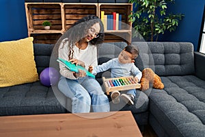 Mother and son reading book sitting on sofa at home