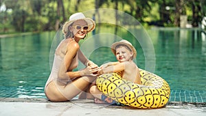 Mother and son relaxing in outdoor swimming pool of tropical resort. Mom and child having fun together, sunbathing. Family summer