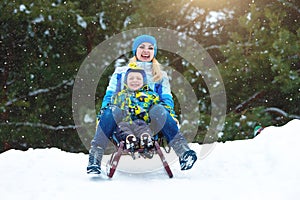 Mother and son ride on sleigh .Child play in snowy forest. Outdoor winter fun for family Christmas vacation.