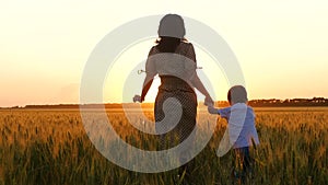 Mother and son run, holding hands. Silhouette of a happy family in a wheat field at sunset.