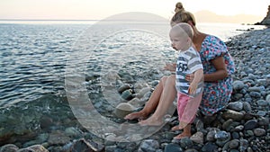 Mother and son sit on the beach at sunset