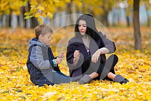 Mother and son sitting amongst yellow fall leaves.