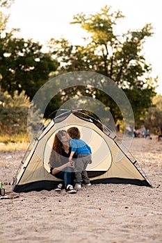 Mother and son sitting in camping tent, admiring sunrise on the river. Family weekend outdoor, local travel on nature