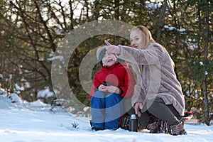 Mother and son sitting on snow in winter forest and communicate