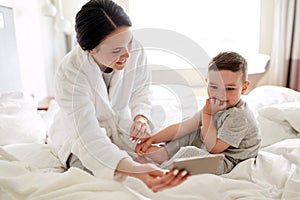 Mother and son with smartphone in bed at hotel