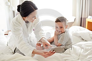 Mother and son with smartphone in bed at hotel