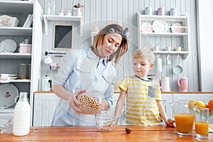 Mother and son are smiling while having a breakfast in kitchen. Mom is pouring milk and corn flakes into glass