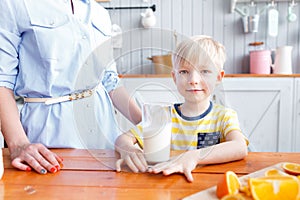 Mother and son are smiling while having a breakfast in kitchen. Mom is pouring milk into glass