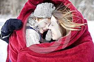 Mother and son snuggling under blanket outside in the snow