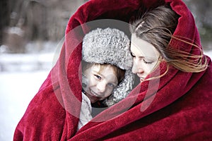 Mother and son snuggling under blanket outside in the snow