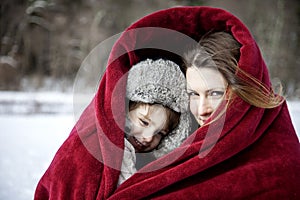 Mother and son snuggling under blanket outside in the snow