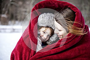 Mother and son snuggling under blanket outside in the snow