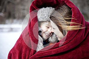 Mother and son snuggling under blanket outside in the snow