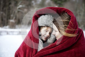 Mother and son snuggling under blanket outside in the snow