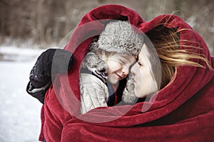 Mother and son snuggling under heart shaped blanket outside in the snow