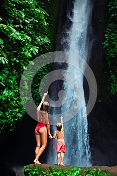 Mother with son stand under waterfall