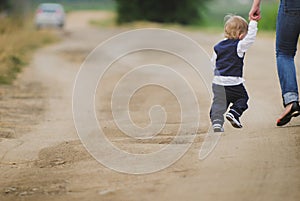 Mother and son take her child along  road forward, she pulls his hand and leads him, the street and good weather