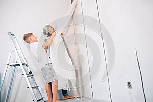 Mother and son take off wallpapers together and prepare room for