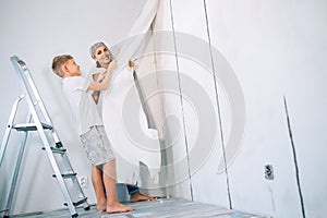 Mother and son take off wallpapers from wall and prepare room for renovation