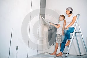 Mother and son take off wallpapers from wall and prepare room for renovation