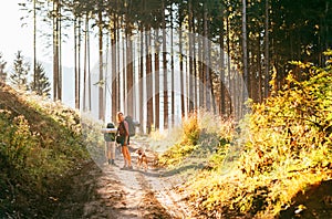 Mother and son with their family member beagle dog walking by the trekking path with backpacks under the evening sun light
