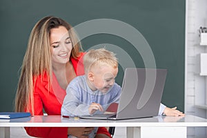 Mother and son together using computer laptop. Little school child son using laptop with mother. Teacher helping school