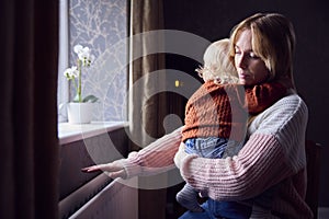 Mother With Son Trying To Keep Warm By Radiator At Home During Cost Of Living Energy Crisis photo