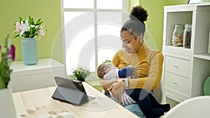 Mother and son using touchpad breastfeeding baby at dinning room