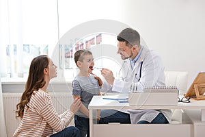 Mother and son visiting pediatrician. Doctor examining little patient`s throat in hospital
