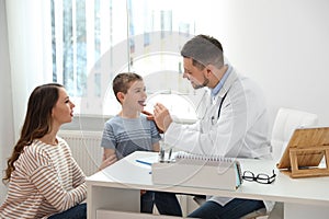 Mother and son visiting pediatrician. Doctor examining patient`s throat in hospital