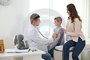Mother and son visiting pediatrician. Doctor examining patient with stethoscope in hospital