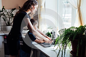 mother and son wash fresh vegetables with water in the kitchen