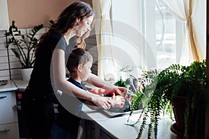 mother and son wash vegetables with water in the sink