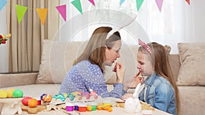 a mother soothes her crying daughter at the table with Easter eggs.