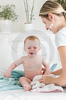 Mother soothing her crying baby boy sitting on bed