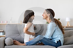 Mother spend time with little daughter talking sitting on couch