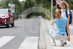 Mother squats on the sidewalk and explains to the little boy how to cross the street safely