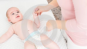 Mother standing next to bed with her newborn baby boy lying on his back. Baby boy on a bed wearing a nappy looking at the mother.