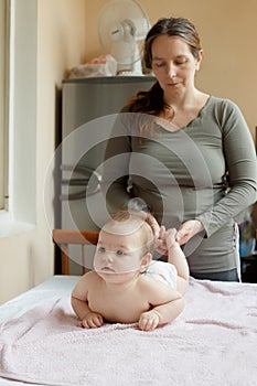 Mother stands next to the child. Massage for the baby. Four month old baby smiling doing gymnastics