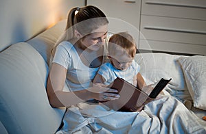 Mother storytelling to her adorable baby boy at bed before going