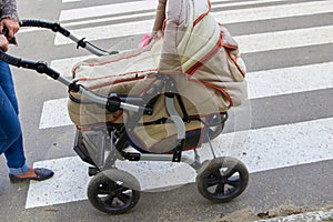 Mother with a stroller at a crosswalk,woman on the street pushes an old stroller on the road