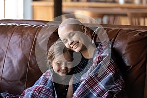 Mother struggling with oncology sitting on sofa embracing small daughter