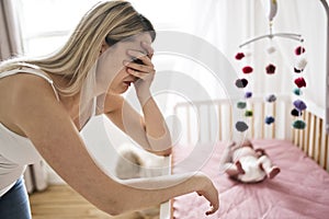 Mother suffering from postnatal depression near crib with cute baby at home