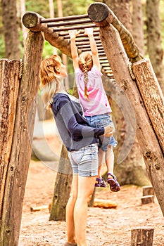 Mother Supporting daughter in the playground with climbing and hanging on a ladder